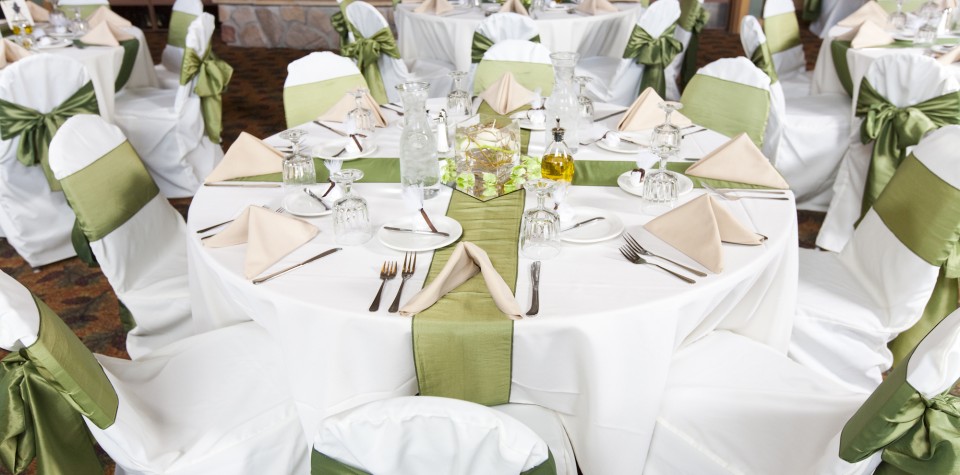 Table setup for a wedding with cloth napkins, silverware, chair covers, and centerpieces