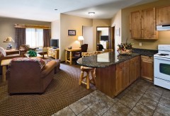 Wide view of a room with a kitchen with an oven and breakfast bar and the living room with sofa, chairs, tv, and desk