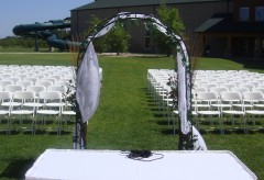 Outdoor wedding ceremony setup with an arch for the couple to stand under and white chairs for the guests